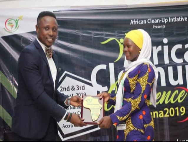 Man in suit presenting certificate award to woman in traditional dress at African Clean-Up Initiative event