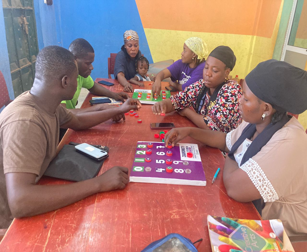 Group of teachers seated around red table demonstrating hands-on math learning activities with eco-friendly materials made from recycled plastic waste